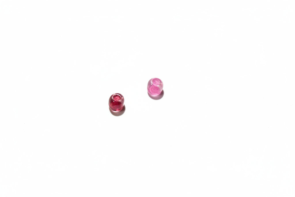 Two small red and pink beads on a gray surface