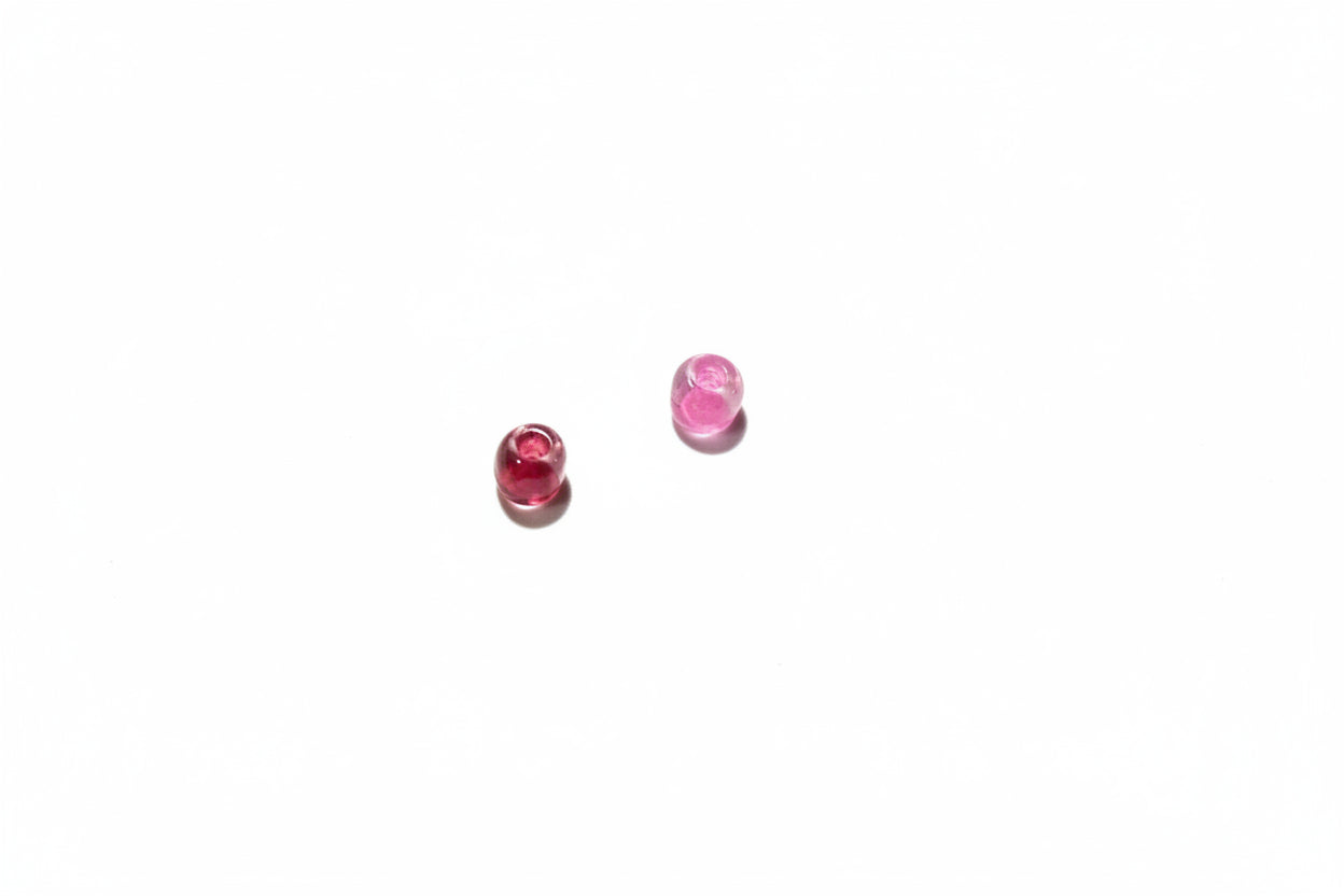 Two small red and pink beads on a gray surface